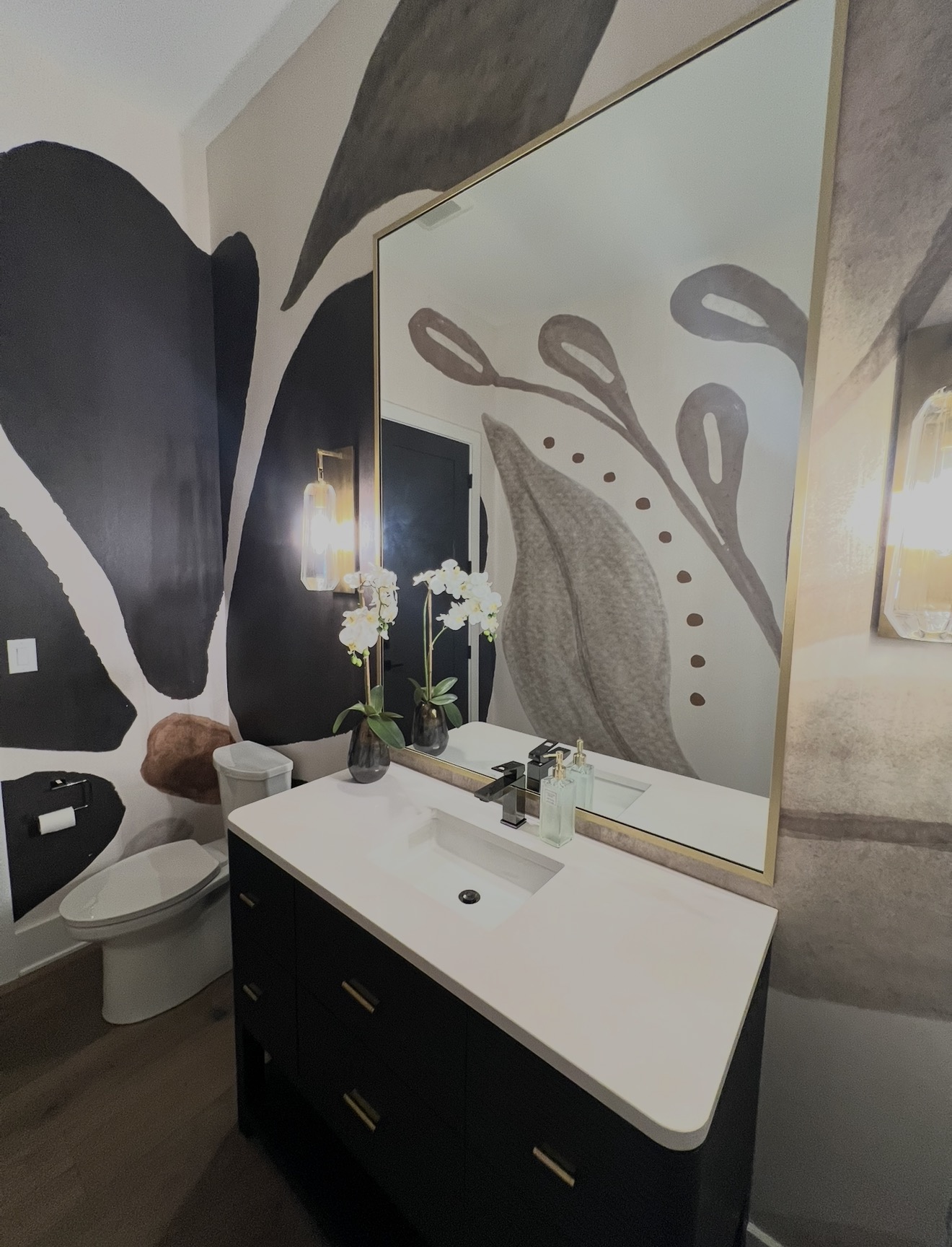 Powder room with hand painted botanical mural, brass framed mirror and black vanity with quartz top