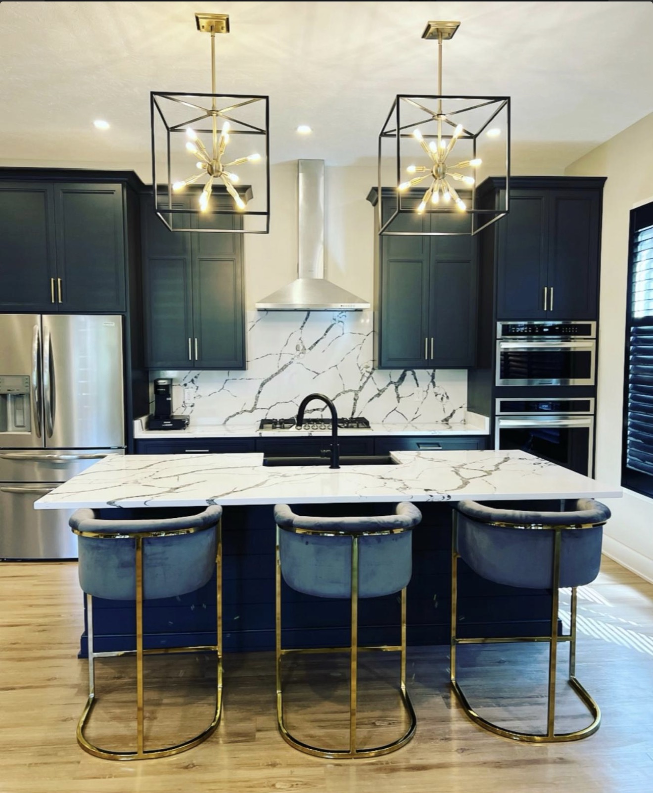 Navy kitchen with quartz waterfall island, brass lantern pendants and marble slab backsplash