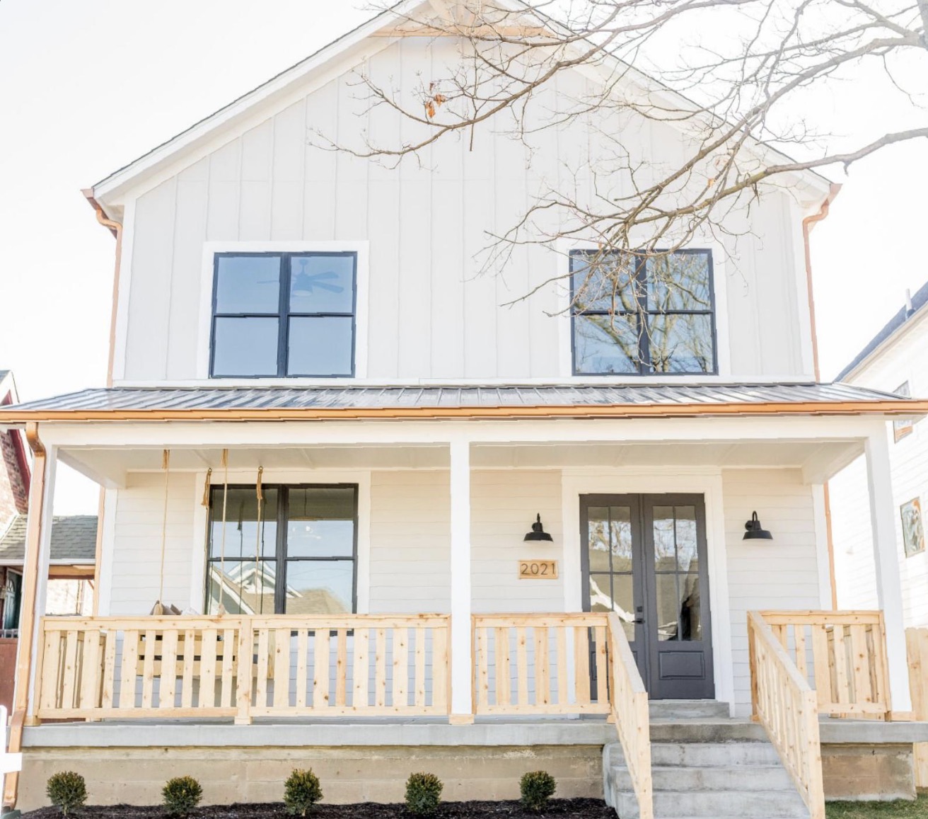 Modern farmhouse custom home with white board and batten siding, standing seam porch roof and cedar railings