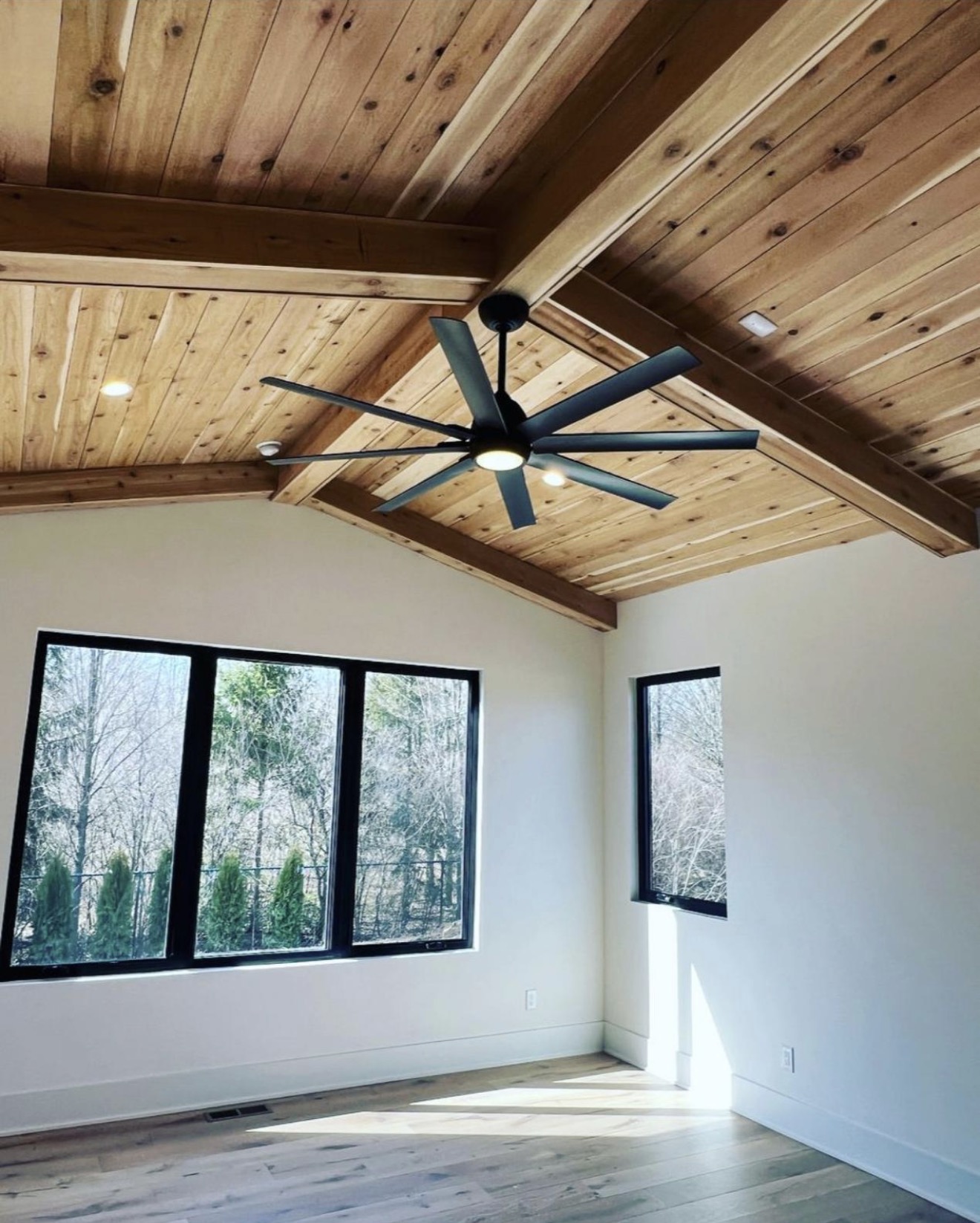 Vaulted bedroom with tongue and groove cedar ceiling, exposed beams and black framed windows to the woods