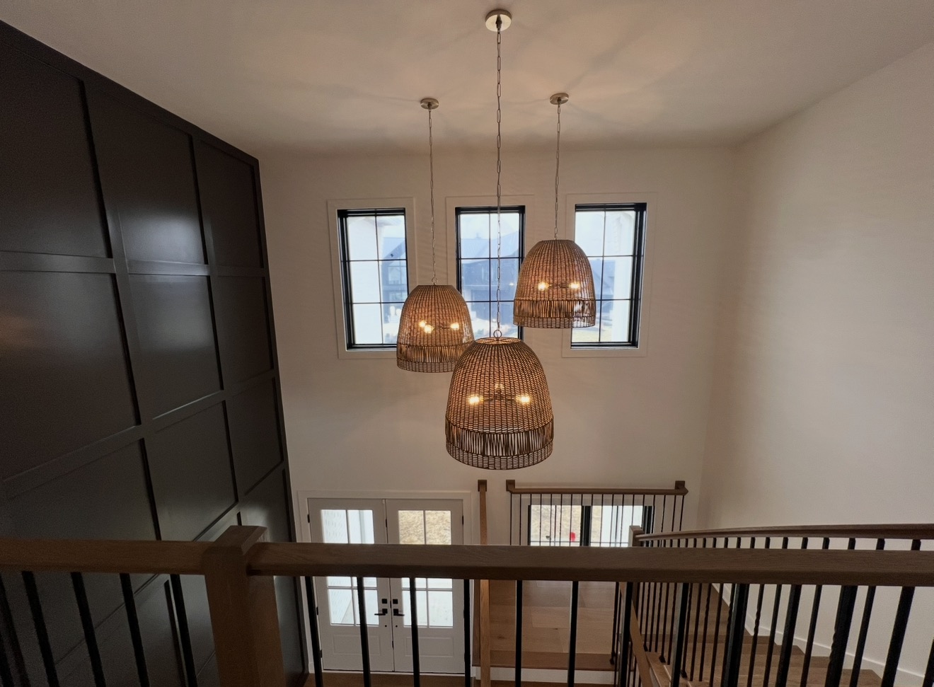 Upper stair landing with woven rattan pendant cluster, black grid paneled wall and oak railing
