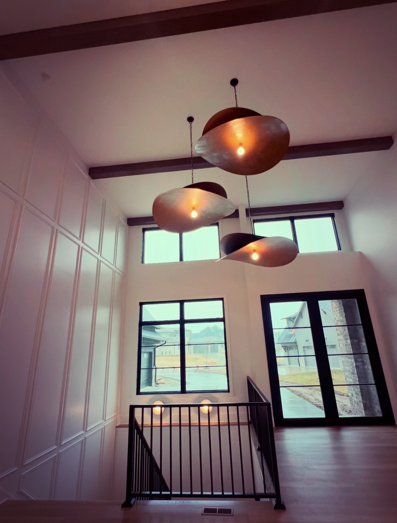 Two story stair hall with paneled millwork, ceiling beams and sculptural plaster pendant lights