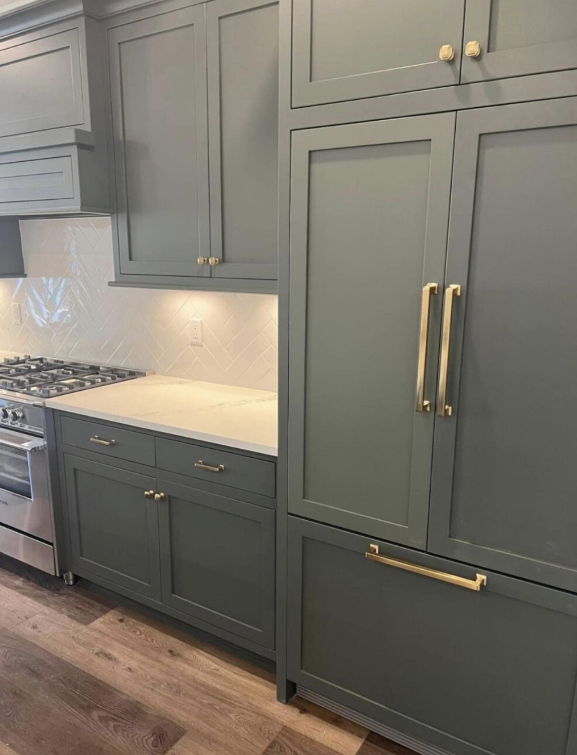 Kitchen with sage green inset cabinetry, brass hardware, herringbone tile backsplash and paneled refrigerator