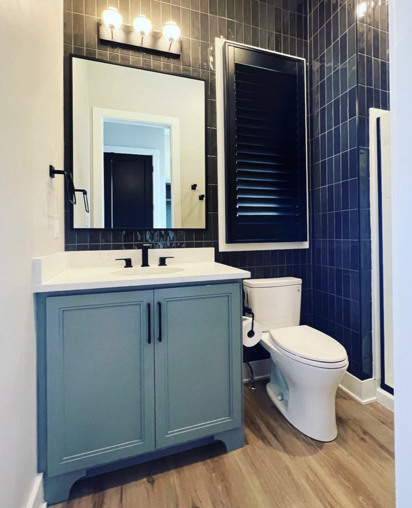 Guest bath with vertical navy gloss tile walls, sea blue vanity and black framed mirror