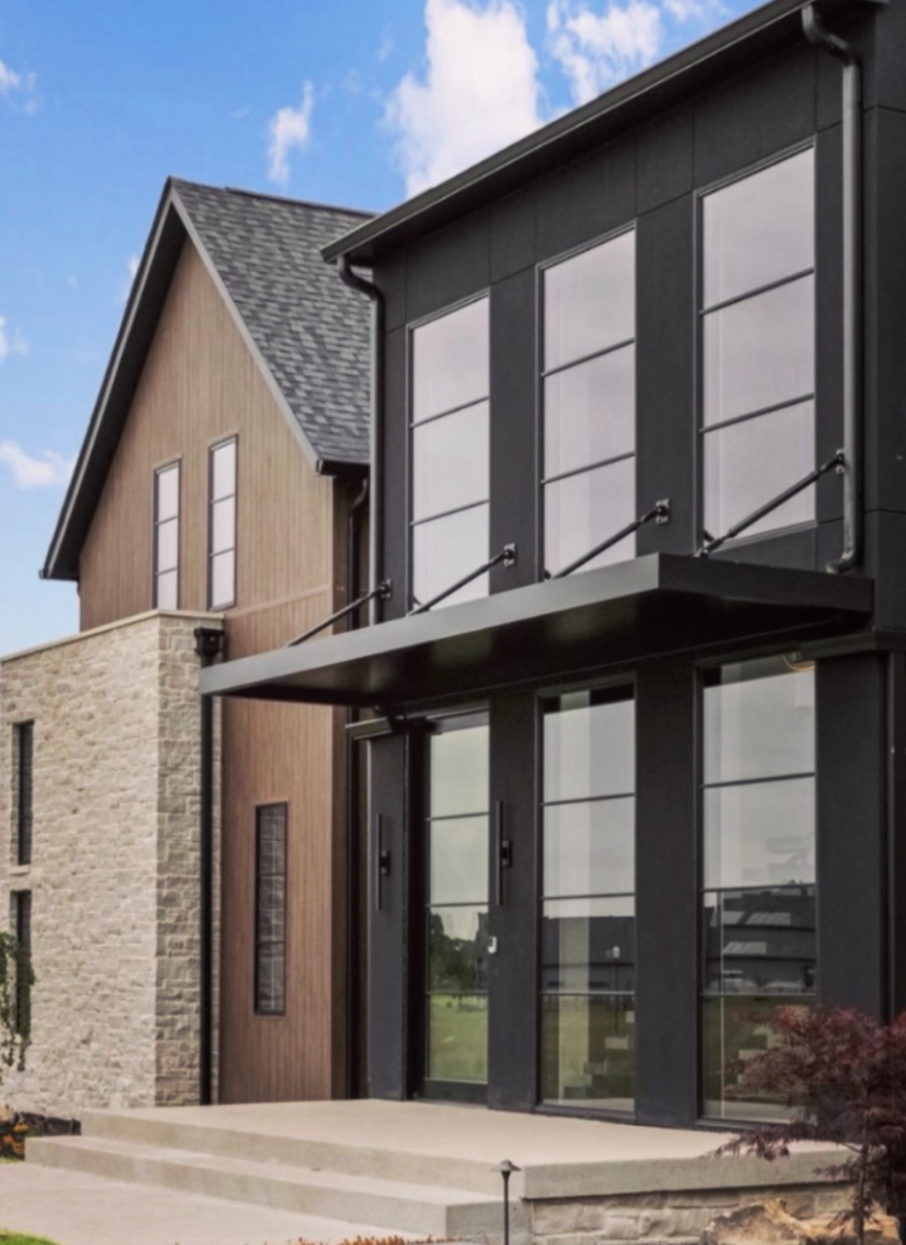 Modern custom home entry with black metal canopy, limestone masonry and warm wood siding