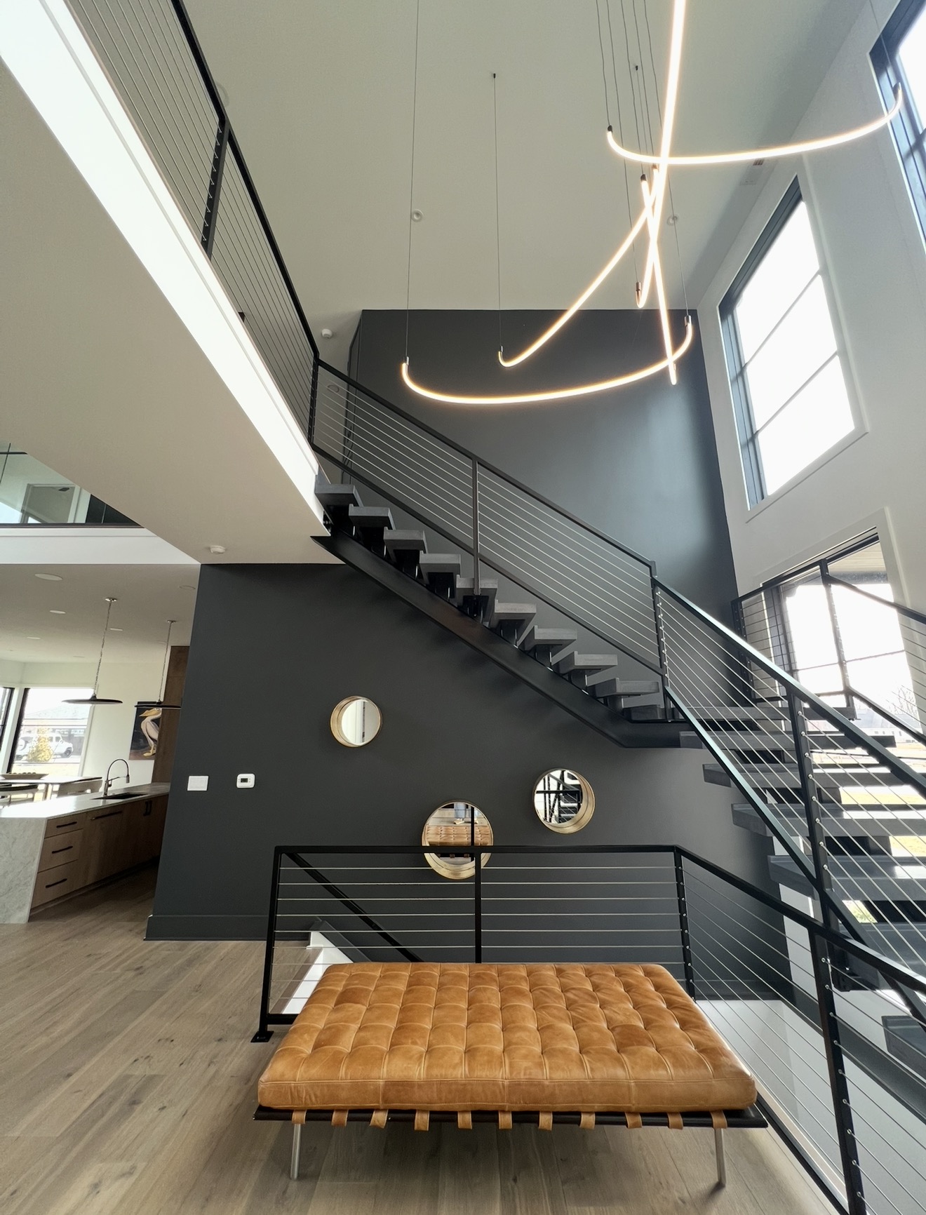 Two story stair hall with sculptural linear chandelier, black accent wall and open sight lines to the kitchen