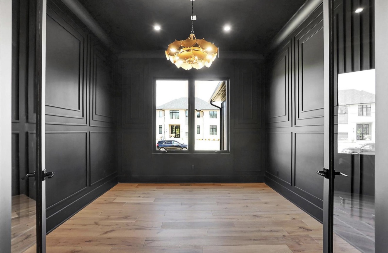 Private study finished in floor to ceiling black paneled millwork with a brass chandelier and glass doors