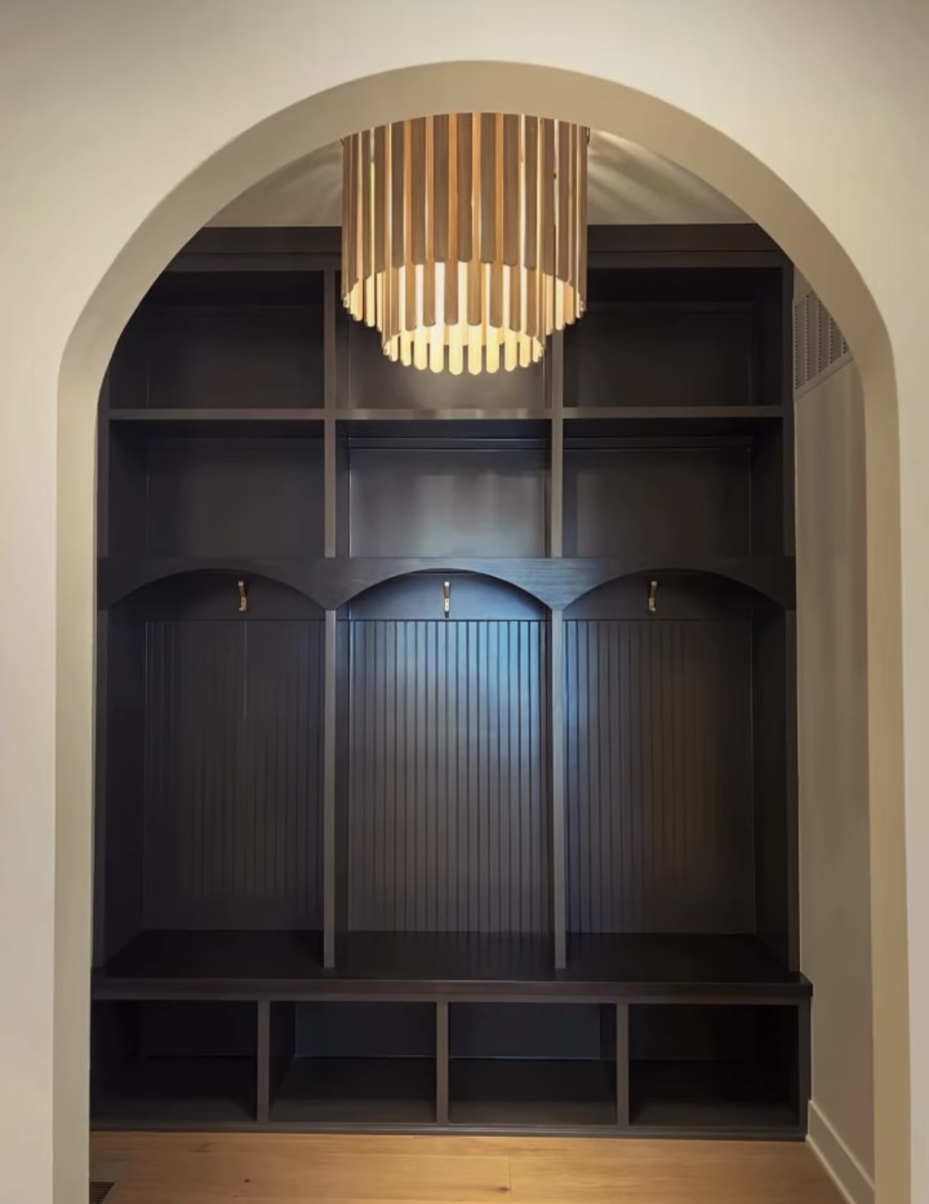 Arched mudroom niche with black fluted lockers, oak bench and a slatted wood drum chandelier