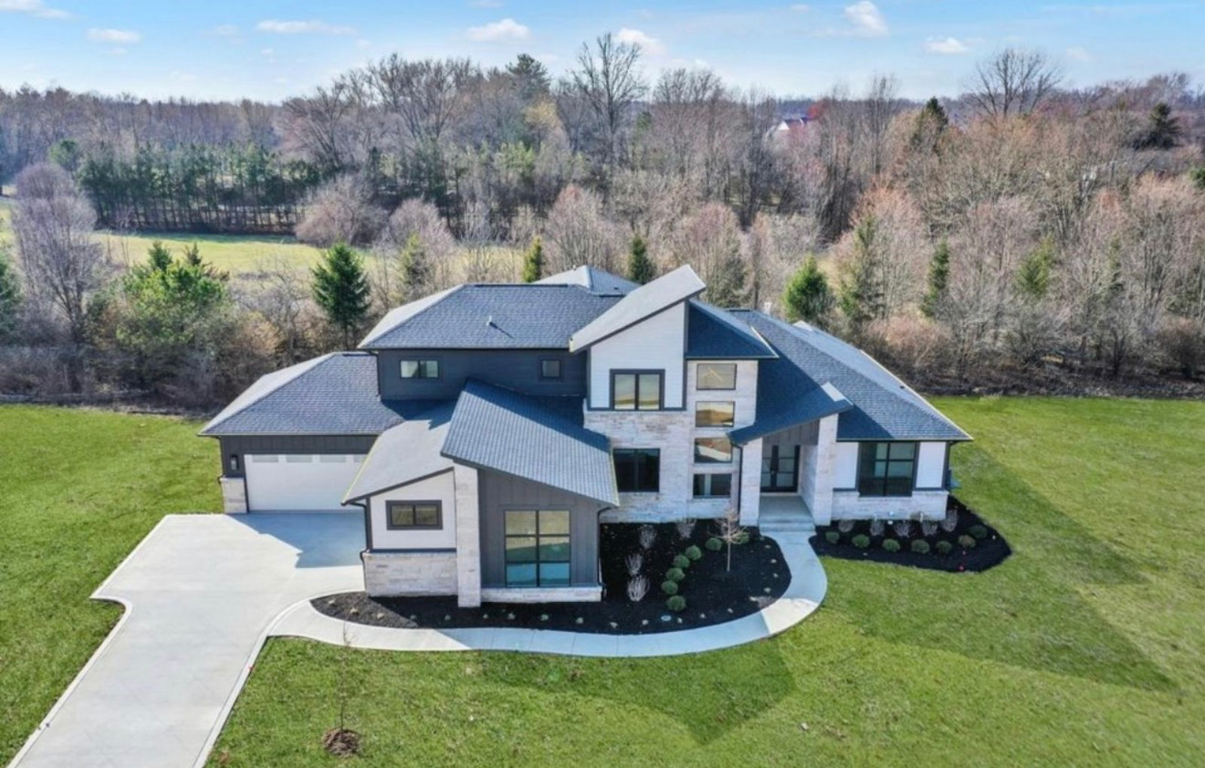 Aerial view of a newly built luxury custom home with stone and shingle siding on a wooded lot near Carmel, Indiana