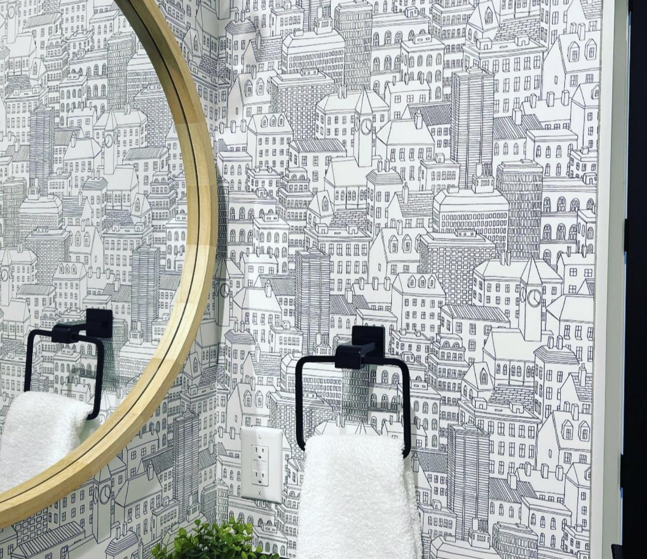 Powder room detail with hand drawn cityscape wallpaper, round white oak mirror and matte black towel rings