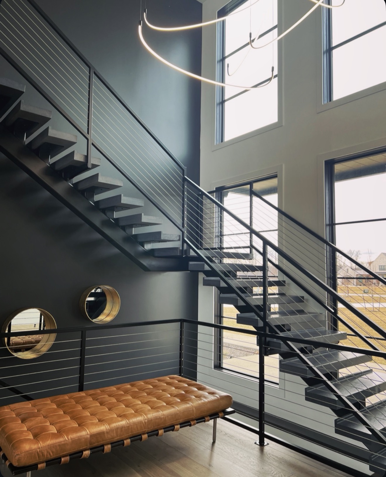 Floating steel and oak staircase with horizontal cable railing against a charcoal two story wall